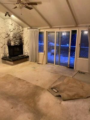 Vaulted living room with carpet and pad removed, bare subfloor, stacked stone fireplace, and sliding glass doors