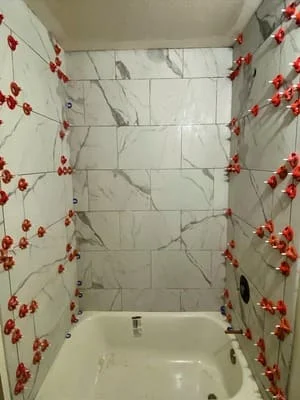 White marble-look large-format tile tub surround with red floral accent trim and chrome fixtures