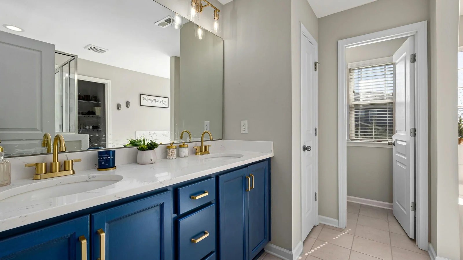 Navy blue double vanity with brass faucets, white quartz countertop, undermount sinks, and gold bar pulls