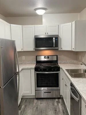 White shaker cabinets, speckled laminate countertops, stainless steel appliances, and gray wood-look vinyl flooring in a remodeled kitchen