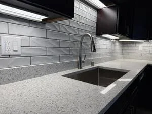 Gray subway tile backsplash, speckled quartz countertop, undermount stainless sink, and brushed nickel pull-down faucet with under-cabinet lighting