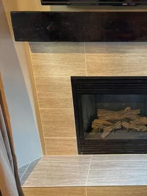 Beige tile fireplace surround with dark wood mantel and black gas insert with faux logs