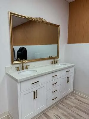 White shaker double vanity with gold hardware, quartz countertop, undermount sinks, and ornate gold-framed mirror