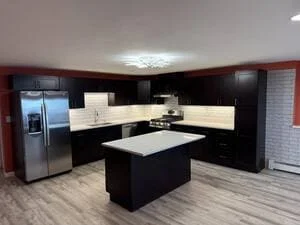Dark shaker cabinets, white subway tile backsplash, quartz island, stainless steel appliances, gray vinyl plank floor