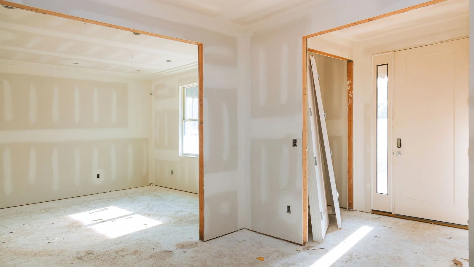Unfinished interior with taped drywall, wood door jambs, white interior doors, and entry door with sidelight