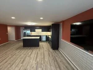 Open kitchen with dark cabinets, black island, quartz countertop, vinyl plank flooring, and terracotta accent wall