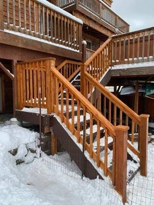 Stained wood deck staircase with vertical baluster railings and snow on the steps in winter
