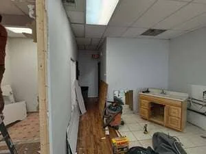 Interior commercial remodel with exposed wood framing, gypsum board walls, oak base cabinet with sink, and drop ceiling
