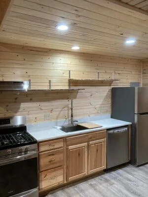 Kitchen with pine tongue-and-groove paneling, honey wood cabinets, gray countertops, stainless steel appliances, and wood shelves