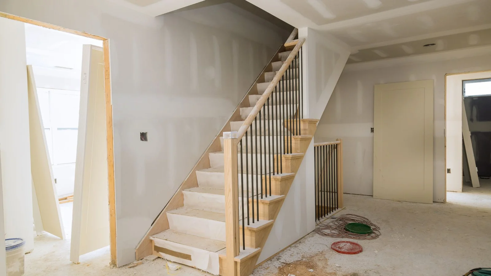 Unfinished staircase with oak treads, oak handrail, and black iron balusters beside drywalled walls
